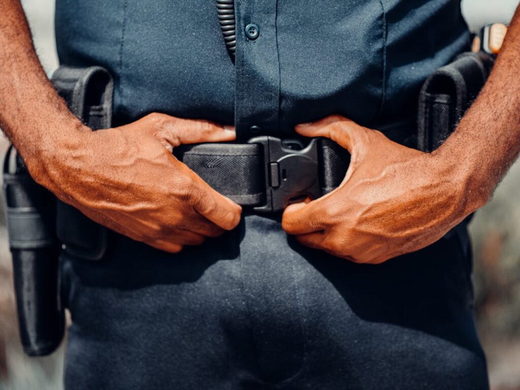 Close-up of a police officer adjusting their duty belt, highlighting law enforcement gear.